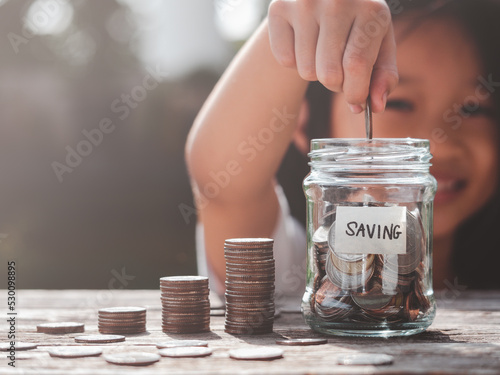 Happy Asian child girl save money by putting coins in glass jar, coin stack growing. Concept saving money, cash, education, growth, finance, bank, investment, management, income, business