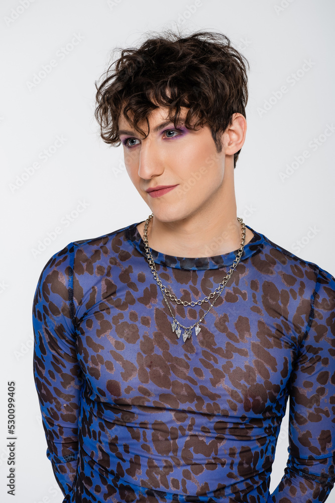 brunette queer model in long sleeve shirt and silver necklaces isolated on grey. brunette queer model in long sleeve shirt and silver necklaces isolated on grey.