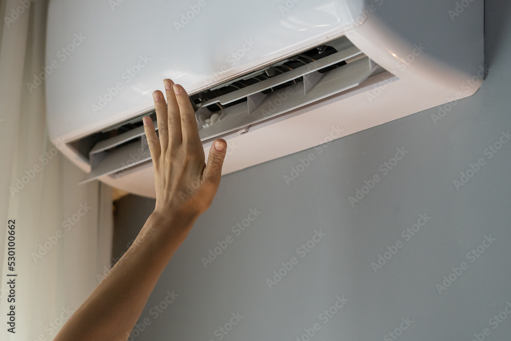 Female owner of apartment stretches hand to check operating air conditioner and catch stream of warm air. Person wants to make flat warm turning on modern device. Landlady enjoys caring about house Female owner of apartment stretches hand to check operating air conditioner and catch stream of warm air. Person wants to make flat warm turning on modern device. Landlady enjoys caring about house