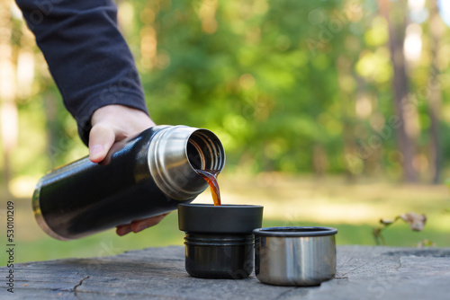 Pouring hot coffee in thermos cups outdoors
