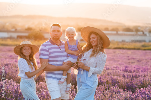 Happy family of young mother and father holding baby girl and teen kid standing in blooming lavender flower meadow outdoor together. Parenthood. Spring season. Childhood. Togetherness.