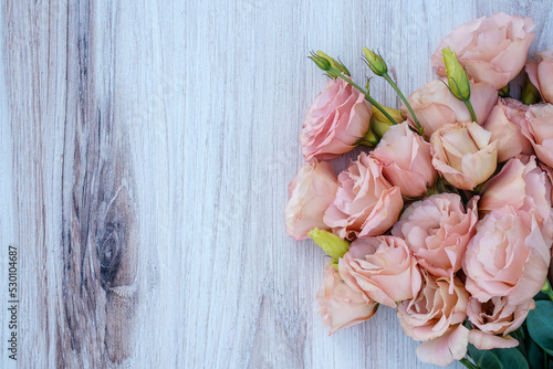 A bunch of apricot lisianthus flowers placed at the right of the image, allowing space for text at the left. Wood background. 