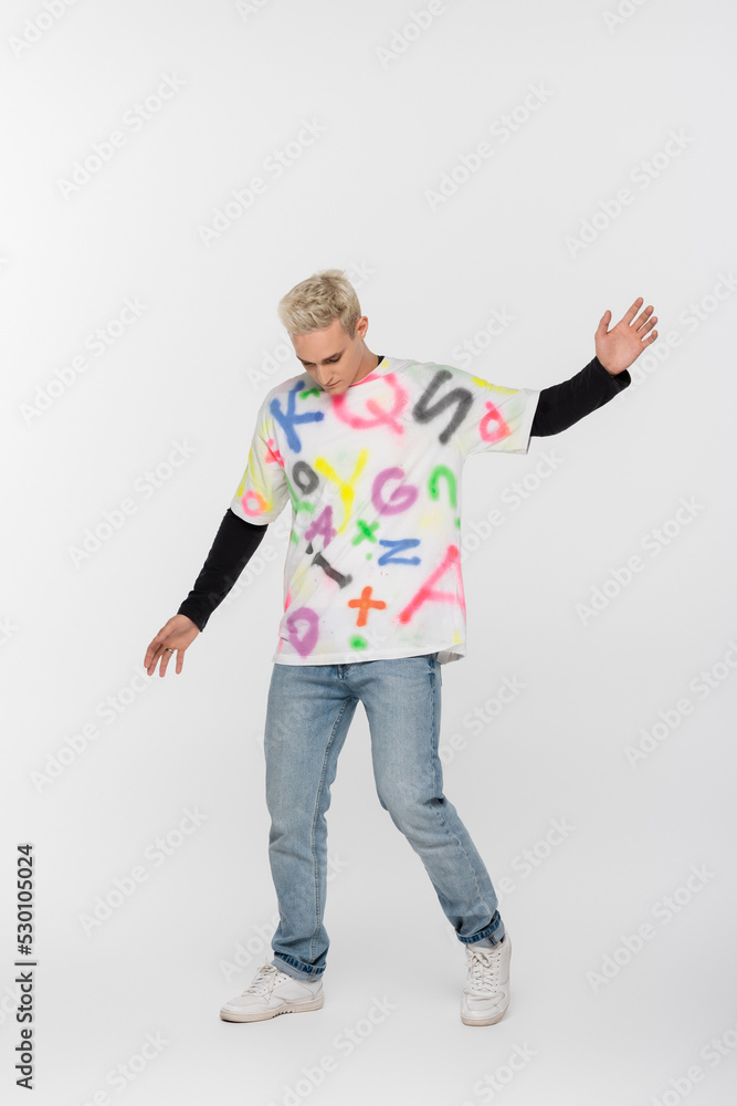 full length of gay man in alphabet print t-shirt posing on grey background. full length of gay man in alphabet print t-shirt posing on grey background.