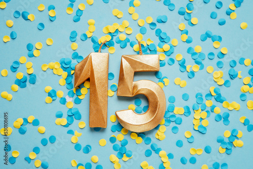 Number 15 fifteen golden celebration birthday candle on yellow and blue confetti Background. fifteen years birthday. concept of celebrating birthday, anniversary, important date, holiday photo