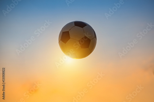 Low angle view of classic black and white ball / soccer football flying in twilight sky. Sport game and athlete concept with no people.