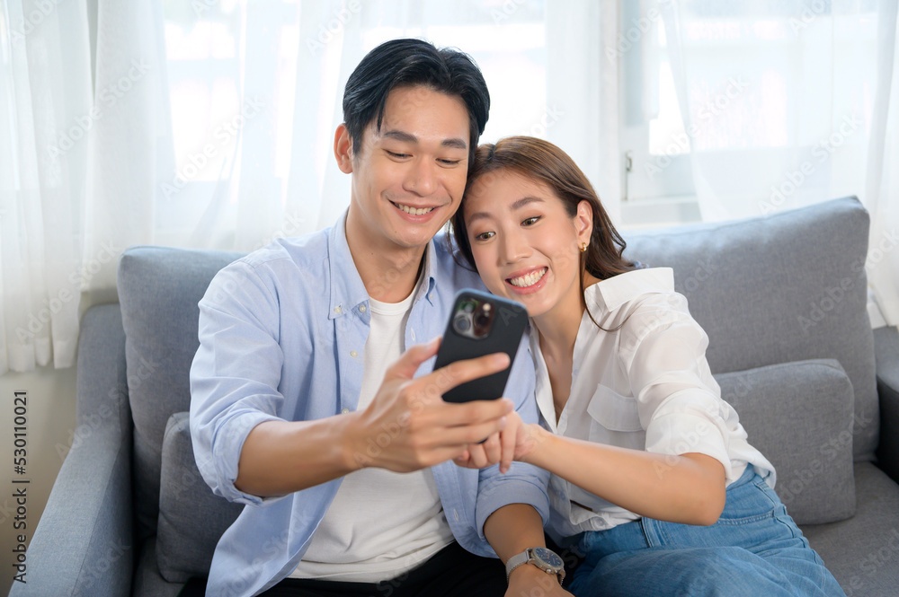 Young smiling asian couple using smartphone in living room at home Young smiling asian couple using smartphone in living room at home