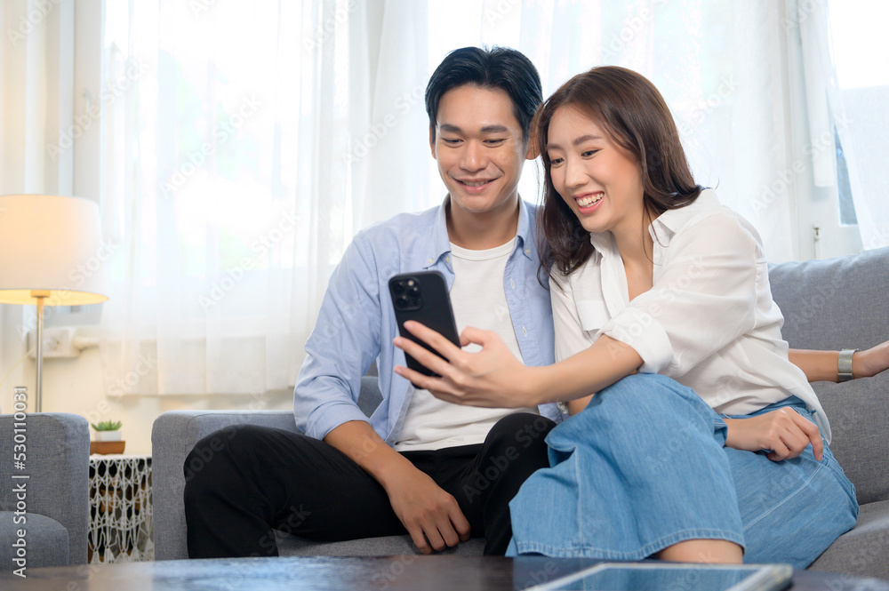 Young smiling asian couple using smartphone in living room at home Young smiling asian couple using smartphone in living room at home