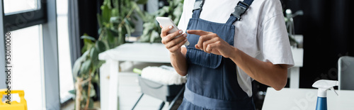 Konstfotografi cropped view of professional cleaner in overalls pointing at mobile phone, banner