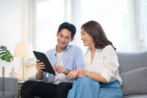 Young smiling asian couple using tablet in living room at home