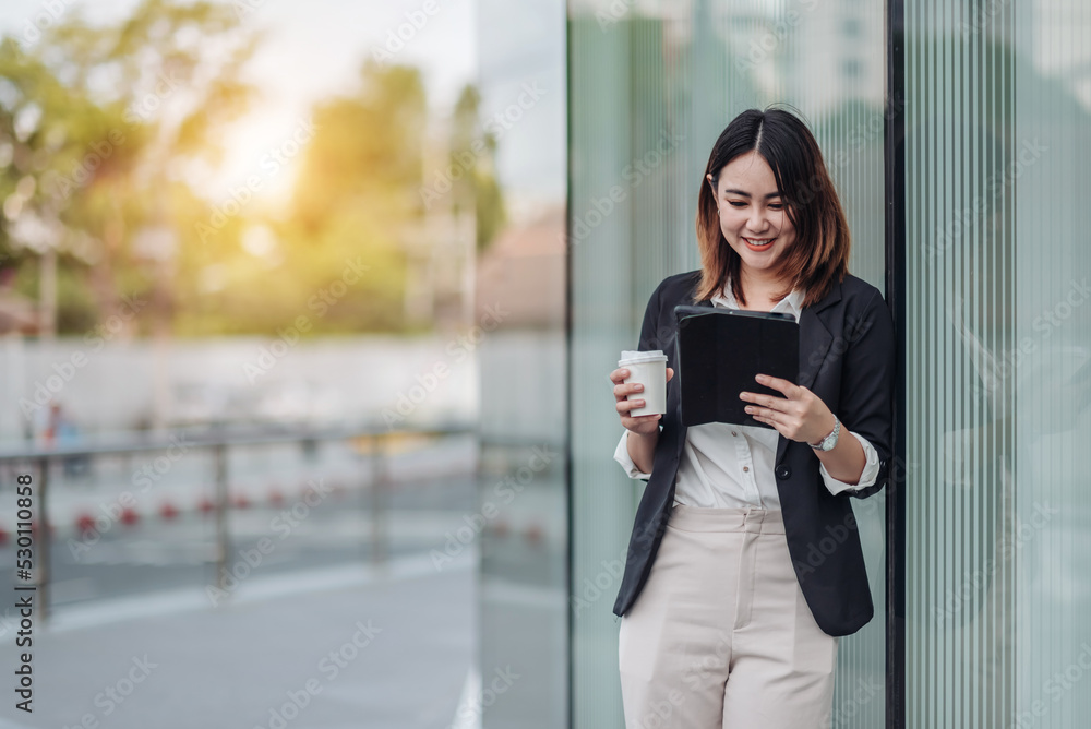Fototapeta premium Young Asian businesswoman talking on phone and sitting in airport before business trip. Beautiful woman passenger has mobile call and discusses something with smile, holds coffee in hand