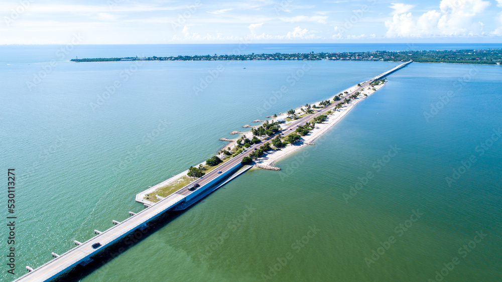 Aerial Drone View Showing the Causeway Bridge in Sanibel, Florida with the Bay and a Preserve in the Foreground and the Gulf of Mexico in the Background Featuring a Blue Sky and Blue Water Aerial Drone View Showing the Causeway Bridge in Sanibel, Florida with the Bay and a Preserve in the Foreground and the Gulf of Mexico in the Background Featuring a Blue Sky and Blue Water