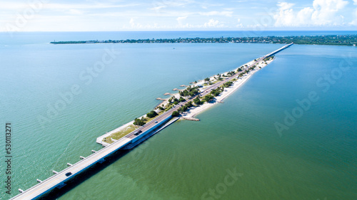 Aerial Drone View Showing the Causeway Bridge in Sanibel, Florida with the Bay and a Preserve in the Foreground and the Gulf of Mexico in the Background Featuring a Blue Sky and Blue Water