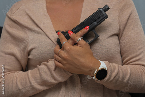 A pistol in female hands at the chest  close-up photo.