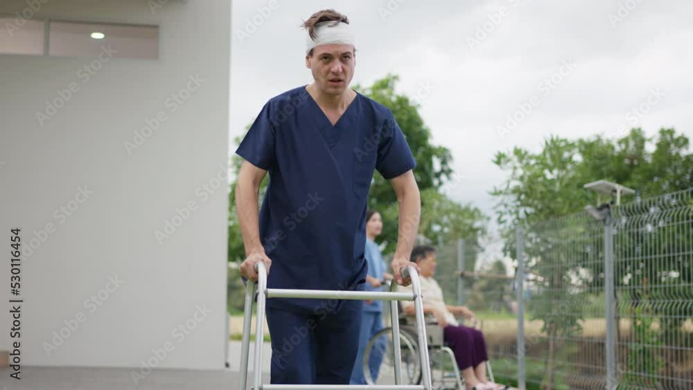 The patient has a bandage on his head using walker and try to walk in the garden at hospital. Physical therapy after accident. Feeling pain during walking. Medical insurance concept. The patient has a bandage on his head using walker and try to walk in the garden at hospital. Physical therapy after accident. Feeling pain during walking. Medical insurance concept.