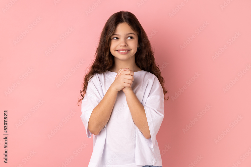 Portrait of smiling happy little girl wearing white T-shirt thinking, dreaming with joyous smiling face, pleasant fantasy, positive hopes. Indoor studio shot isolated on pink background. Portrait of smiling happy little girl wearing white T-shirt thinking, dreaming with joyous smiling face, pleasant fantasy, positive hopes. Indoor studio shot isolated on pink background.