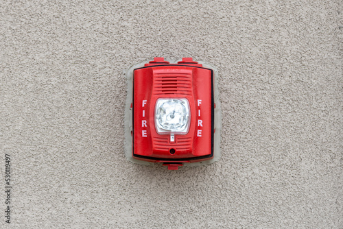 Red fire alarm siren with flashing light strobe isolated on gray cement wall outdoor. Fire safety. photo