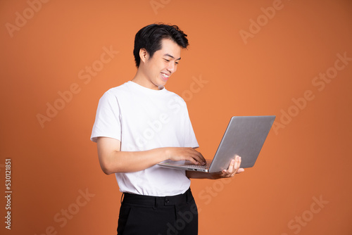 asian man holding laptop, isolated on orange background