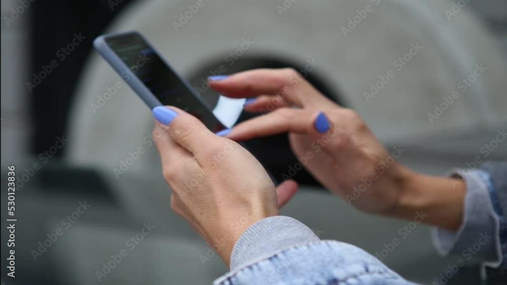 Finger of woman with blue manicure touching scroll page app on mobile phone. Girl in a denim jacket search and browsing movie video in the internet library to watch film online in outdoor Finger of woman with blue manicure touching scroll page app on mobile phone. Girl in a denim jacket search and browsing movie video in the internet library to watch film online in outdoor