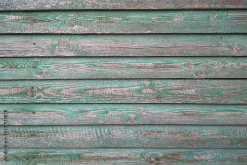 The texture of an old peeling wall made of wooden boards. Wooden boards painted green, faded and faded from wind and rain. Old rough wood, wood. The outer wall.