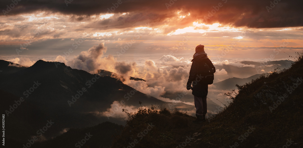 Obraz premium female tourist with a backpack in autumn on the mountain with outstretched arms welcomes admires the sunset