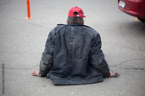 Homeless man sits on the road. A man without housing sits on the sidewalk. Man has lost the ability to walk. photo