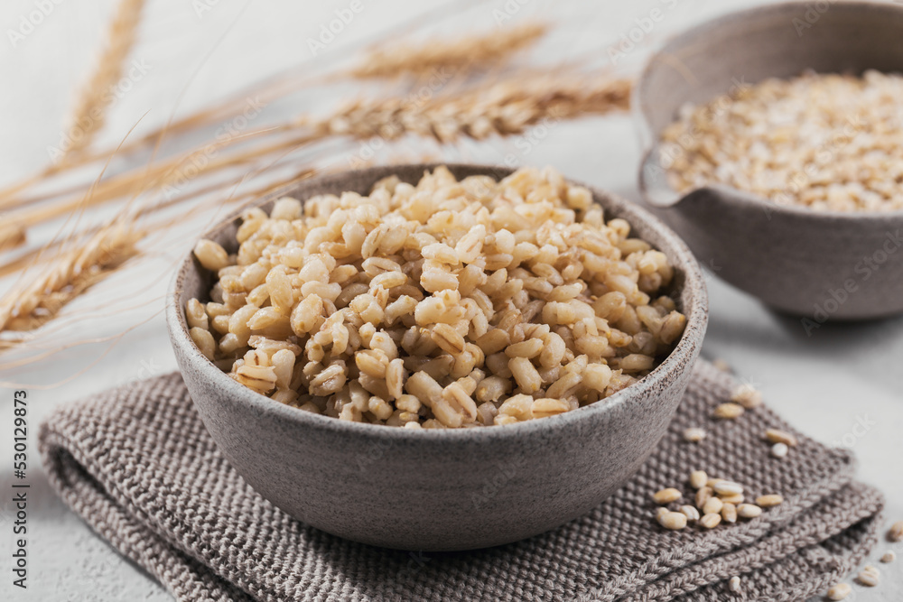 Bowl of cooked peeled barley grains porridge with ears of wheat on white background. Cooking Healthy and diet food concept. Bowl of cooked peeled barley grains porridge with ears of wheat on white background. Cooking Healthy and diet food concept.