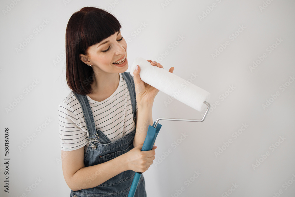 Young woman, who have finally collected the necessary amount of funds for repairs, rejoice and dance. Instead of real microphone, girl using into a mop and a paint roller. Young woman, who have finally collected the necessary amount of funds for repairs, rejoice and dance. Instead of real microphone, girl using into a mop and a paint roller.