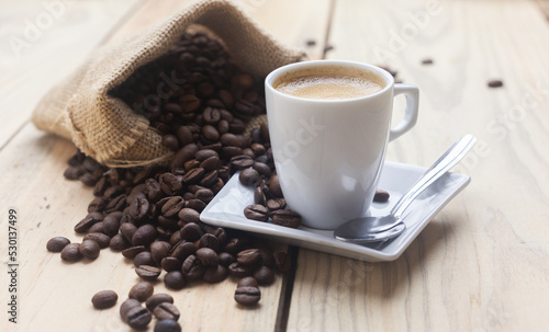 Taza de cafe caliente junto a un saco de tela con granos de café