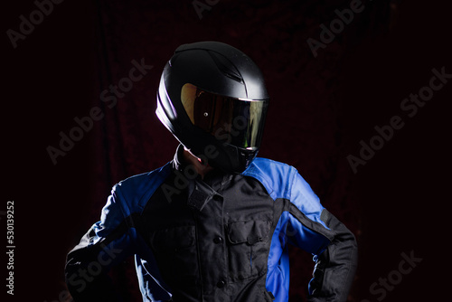 man in a motorcycle helmet in an outfit on a dark studio background. © velimir