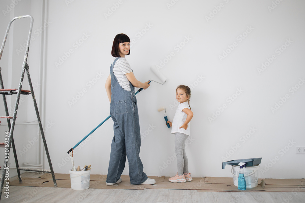 Full length portrait back view of young mother and her small cute daughter enjoying time together while painting wall. Full length portrait back view of young mother and her small cute daughter enjoying time together while painting wall.