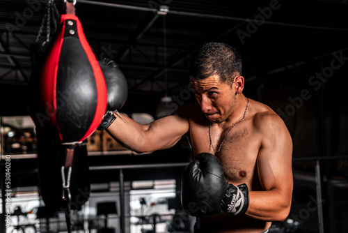 High quality photography. Shirtless Hispanic man with a pear and boxing gloves punching hard while making a face.