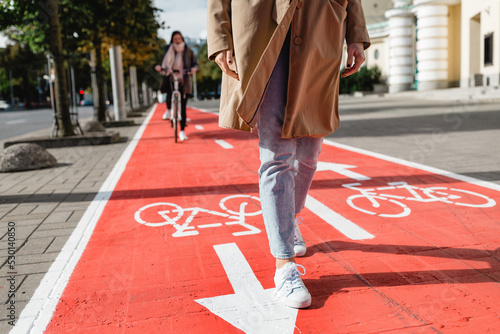 people, city and traffic concept - close up of woman's feet walking along separate bike lane or red road with signs only for bicycles on street photo