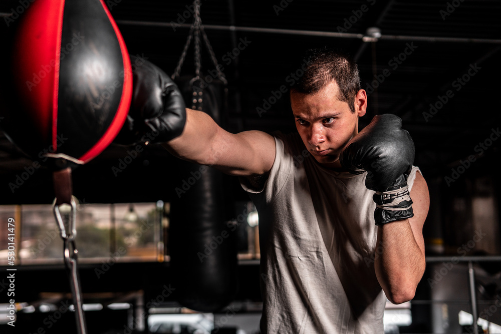 High quality photography. A short-haired Caucasian man throwing a punch at a punching bag. The man is wearing a gray sleeveless shirt. High quality photography. A short-haired Caucasian man throwing a punch at a punching bag. The man is wearing a gray sleeveless shirt.