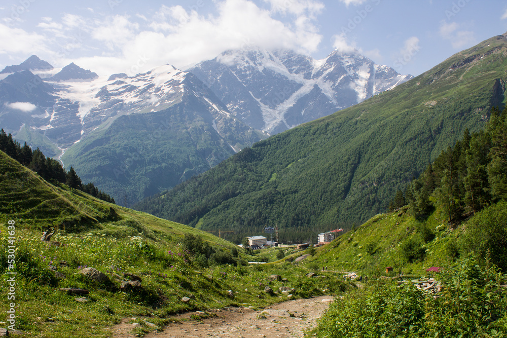 Panoramic view of the village of Terskol with residential buildings among the high slopes of mountains with glaciers on the tops on a sunny summer day in the Elbrus region in the North Caucasus