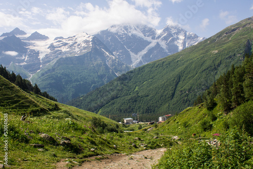Panoramic view of the village of Terskol with residential buildings among the high slopes of mountains with glaciers on the tops on a sunny summer day in the Elbrus region in the North Caucasus
