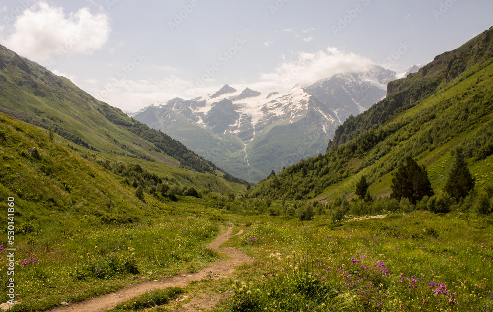 Beautiful landscape - the slopes of high mountains and the green Alpine valley of Terskol with a walking path in the Elbrus region in Kabardino-Balkaria on a clear summer sunny day