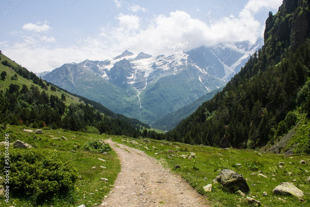 Beautiful landscape - the slopes of high mountains and the green Alpine valley of Terskol with a walking path in the Elbrus region in Kabardino-Balkaria on a clear summer sunny day