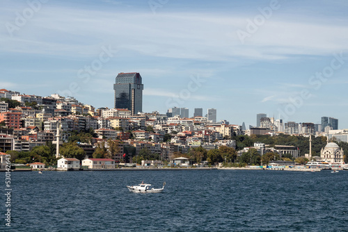 View of a small fishing boat on Bosphorus and Gunussuyu area of Beyoglu district in Istanbul. It is a sunny summer day. © theendup