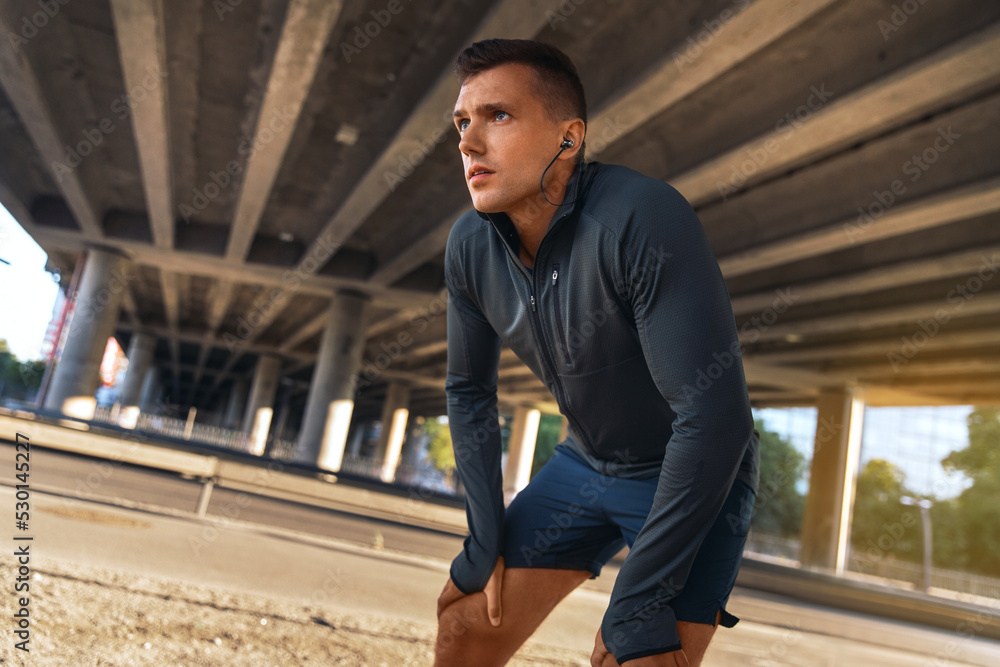 fitness, sport and training concept - tired young man in earphones doing sports outdoors fitness, sport and training concept - tired young man in earphones doing sports outdoors