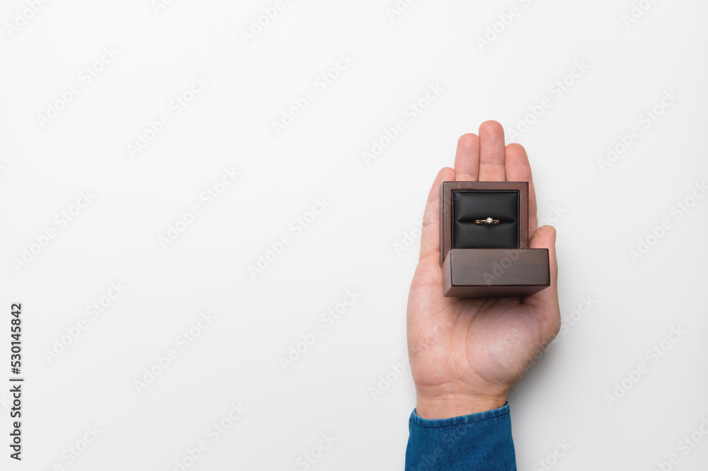 a man's hand holds a diamond engagement ring in a wooden elegant box, making a marriage proposal a man's hand holds a diamond engagement ring in a wooden elegant box, making a marriage proposal