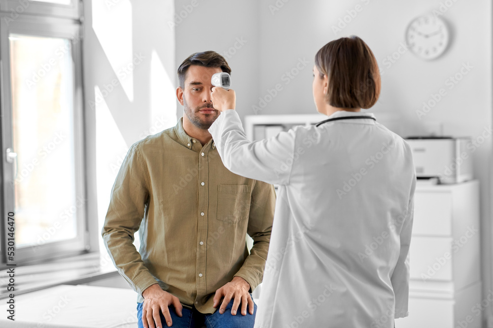 Fototapeta premium medicine, healthcare and people concept - female doctor with infrared forehead thermometer measuring temperature of man patient at hospital