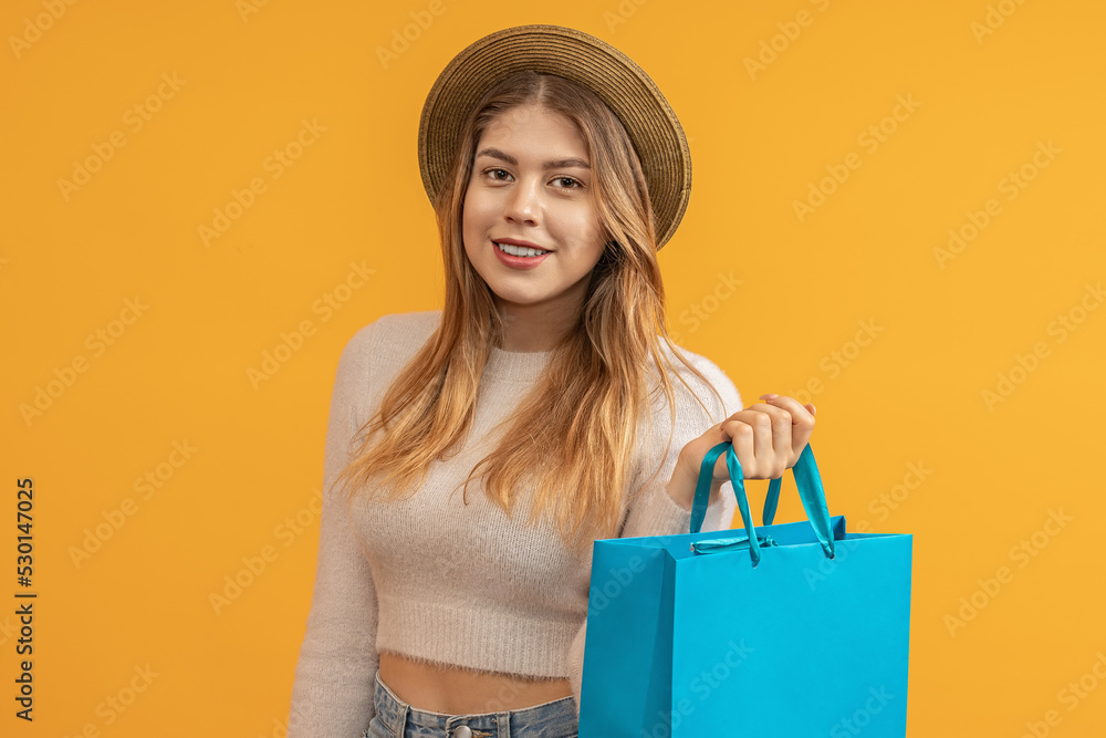 stylish young girl in a summer hat with a shopping bag in her hand on a yellow background