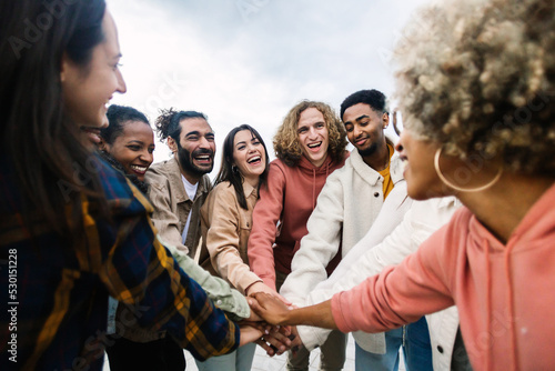 Happy young group of multiracial people stacking hands outdoors - Community and unity concept photo