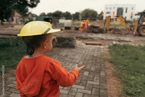 Child with excavator near construction site, dreams to be an engineer. Little builder. Education, and imagination, purposefulness concept