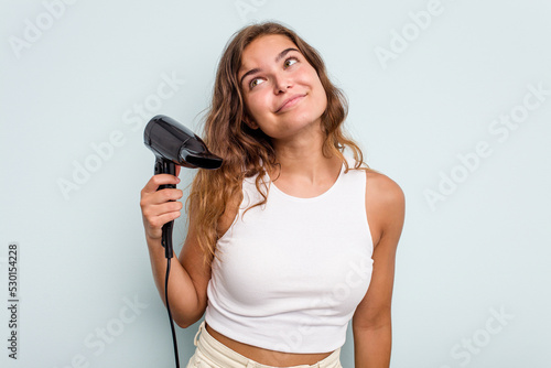 Young caucasian woman holding a hairdryer isolated on blue background dreaming of achieving goals and purposes