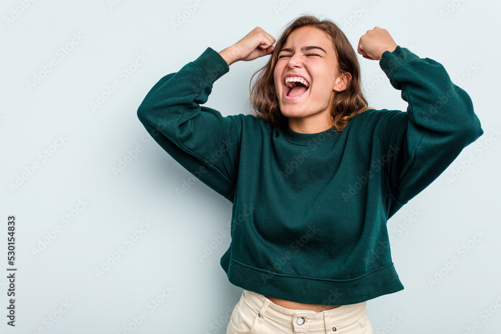 Young caucasian woman isolated on blue background raising fist after a victory, winner concept. Young caucasian woman isolated on blue background raising fist after a victory, winner concept.