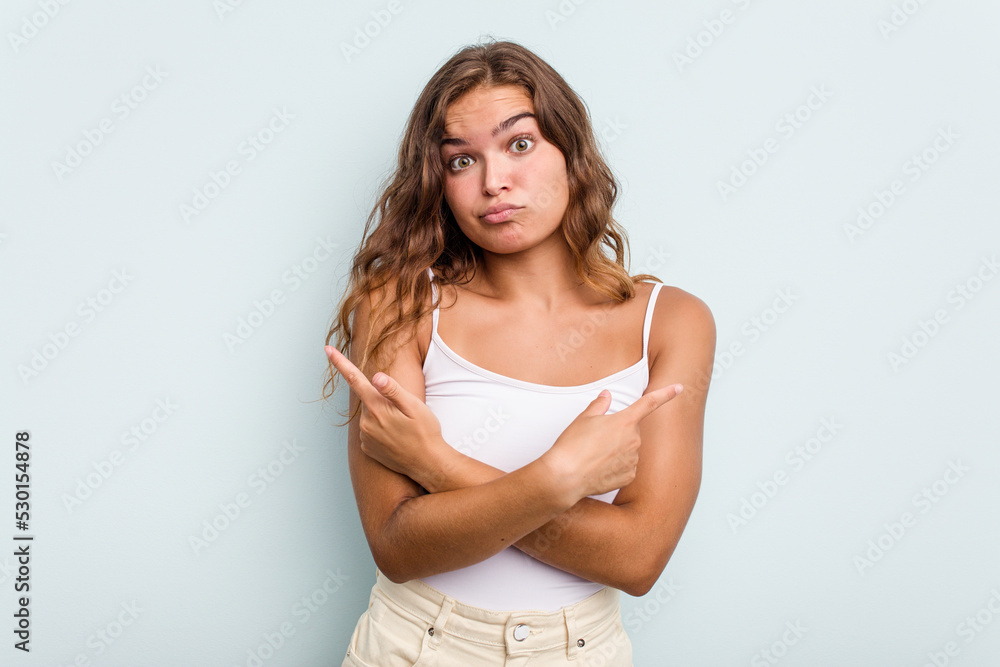 Young caucasian woman isolated on blue background points sideways, is trying to choose between two options. Young caucasian woman isolated on blue background points sideways, is trying to choose between two options.
