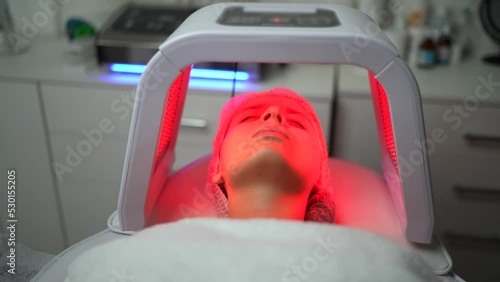 Close up of young woman having red and blue LED light facial therapy treatment in beauty salon. Woman laying on a couch and relaxing while LED light session. Beauty, healthcare and wellness concept.