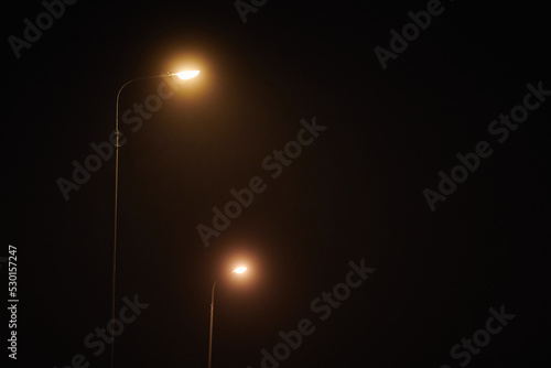 Two night lamppost shines with faint mysterious yellow light through evening fog at quiet night photo