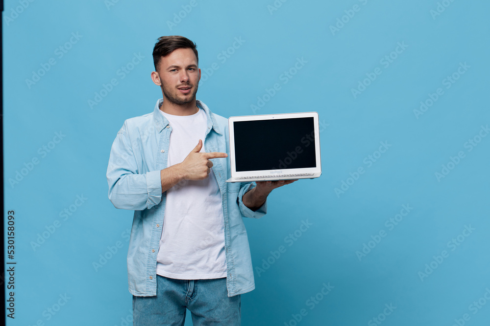 Smiling happy tanned handsome man in casual basic t-shirt point finger at new purchase laptop posing isolated on blue studio background. Copy space Banner Mockup. Electronics repair IT concept